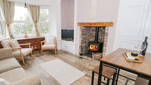 A cozy living room with a fireplace, wooden furniture, and a TV. - Ty Arth (Llandudno)