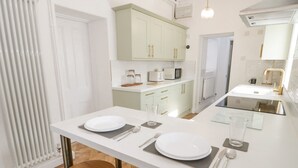 A modern kitchen with white countertops, a central island with two stools, and light green cabinets. - Ty Arth (Llandudno)