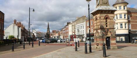 A historic town square with cobblestone pavement, traditional buildings, and a prominent clock tower.