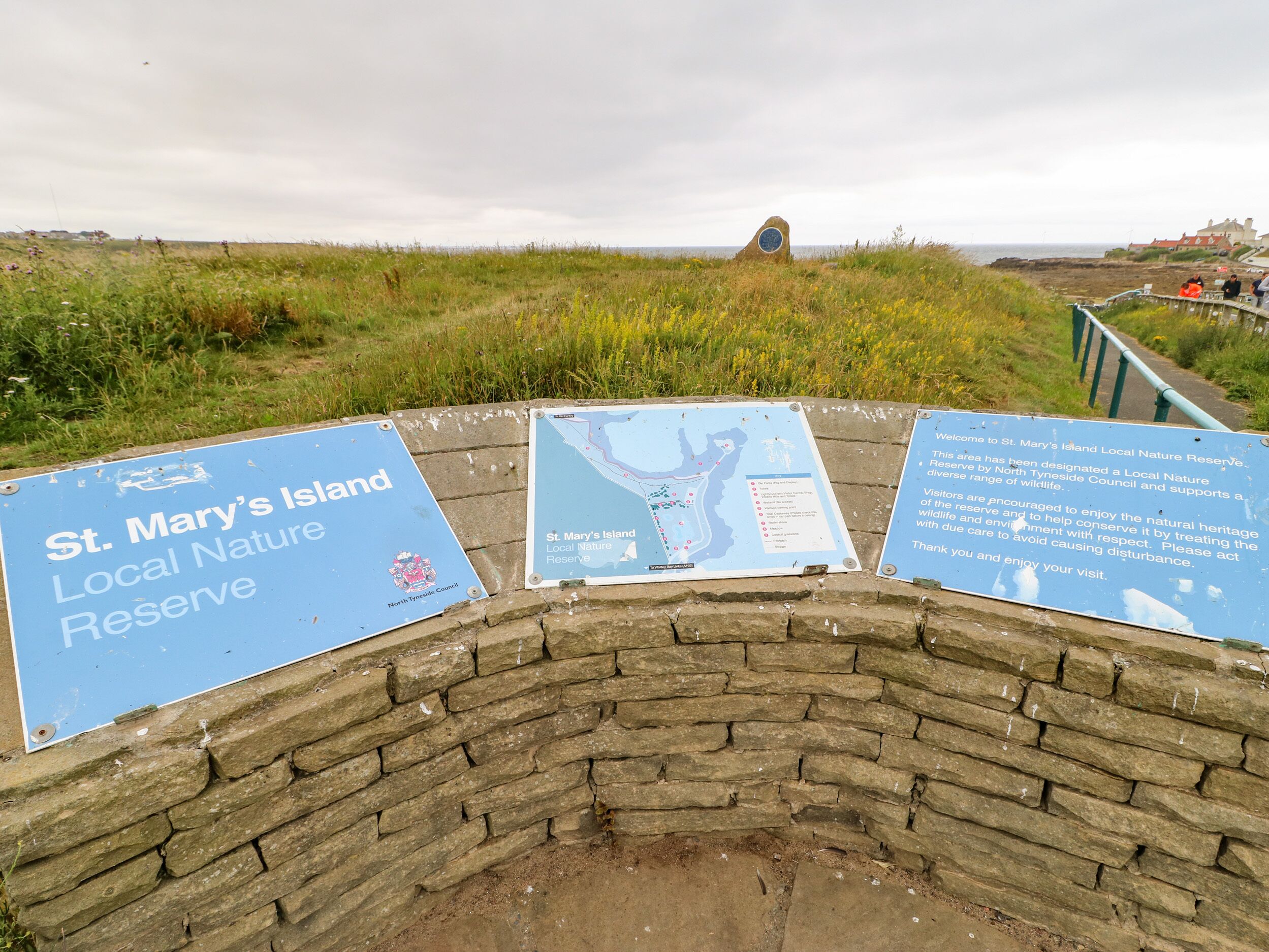 A stone wall with signs for St. Mary's Island Local Nature Reserve, including a map and visitor information.