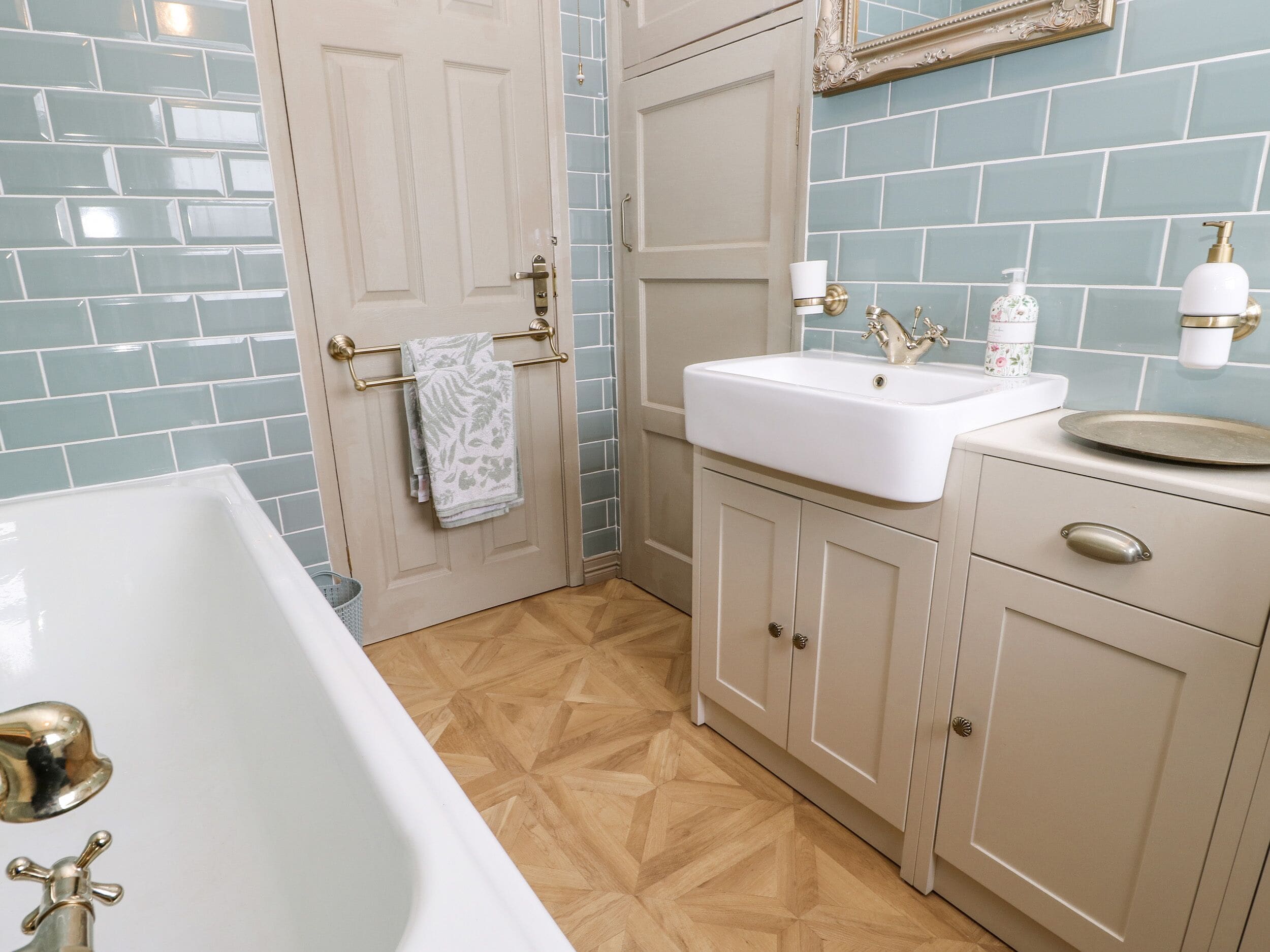 Un baño con una bañera blanca, un lavabo con grifo dorado y un espejo sobre el lavabo.