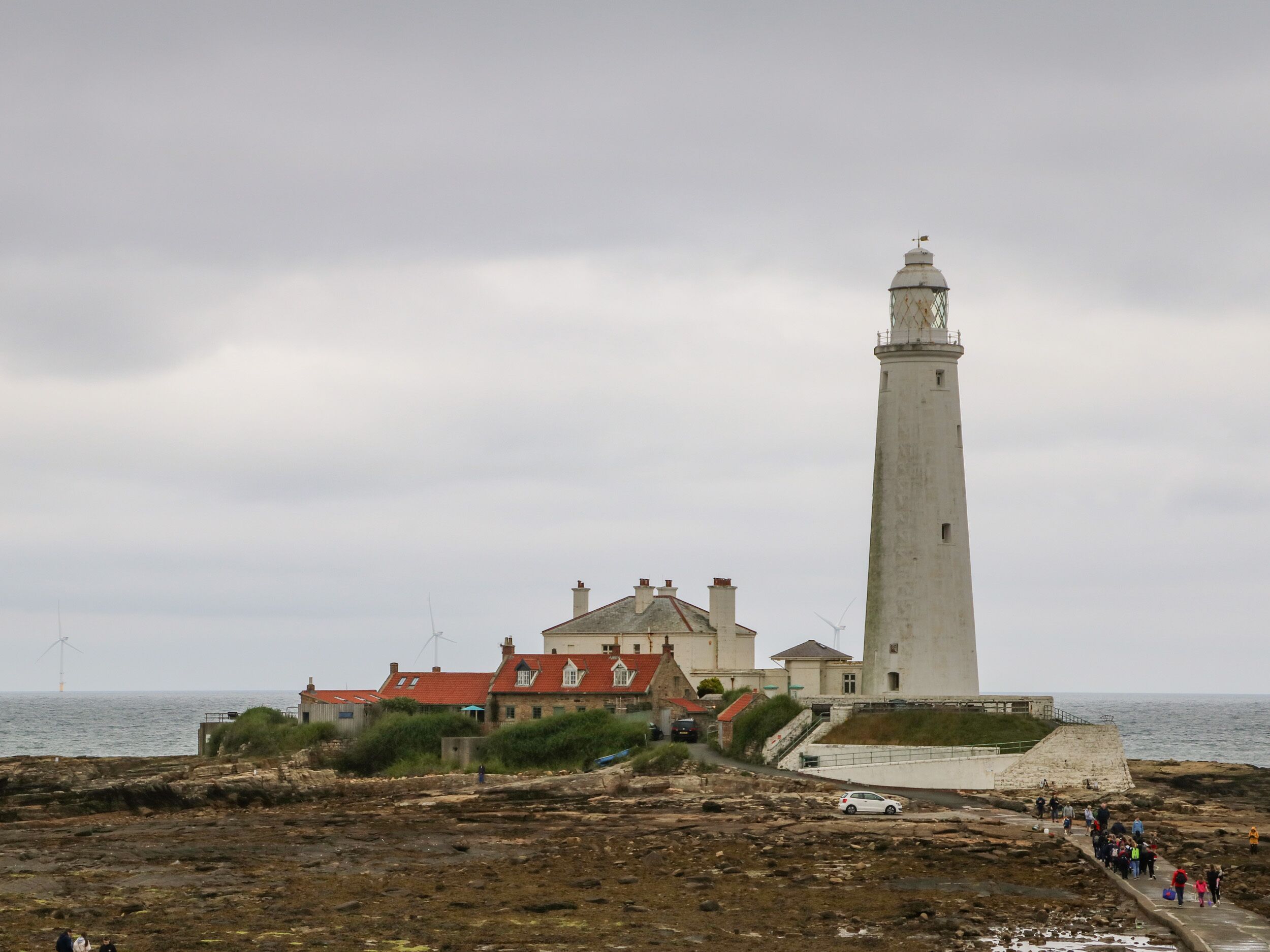 A lighthouse with a tall, narrow tower and a shorter building with a red roof nearby.