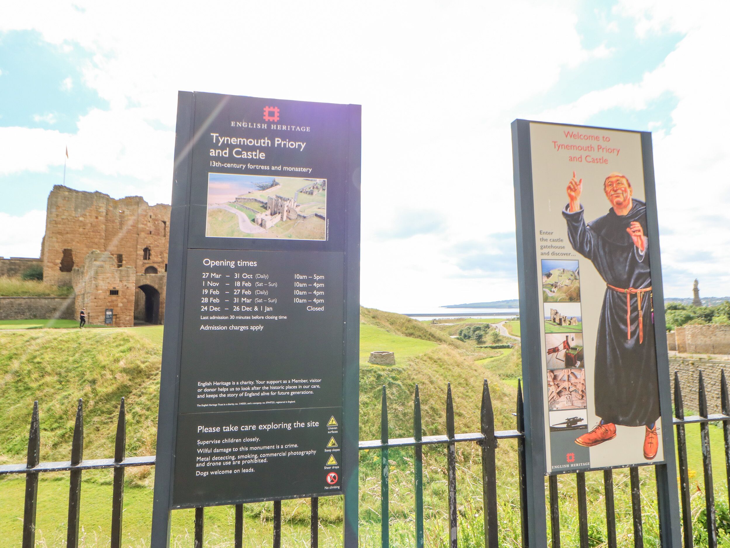 Un cartel informativo sobre el priorato y castillo de Tynemouth, con horarios de apertura y un mensaje de bienvenida.