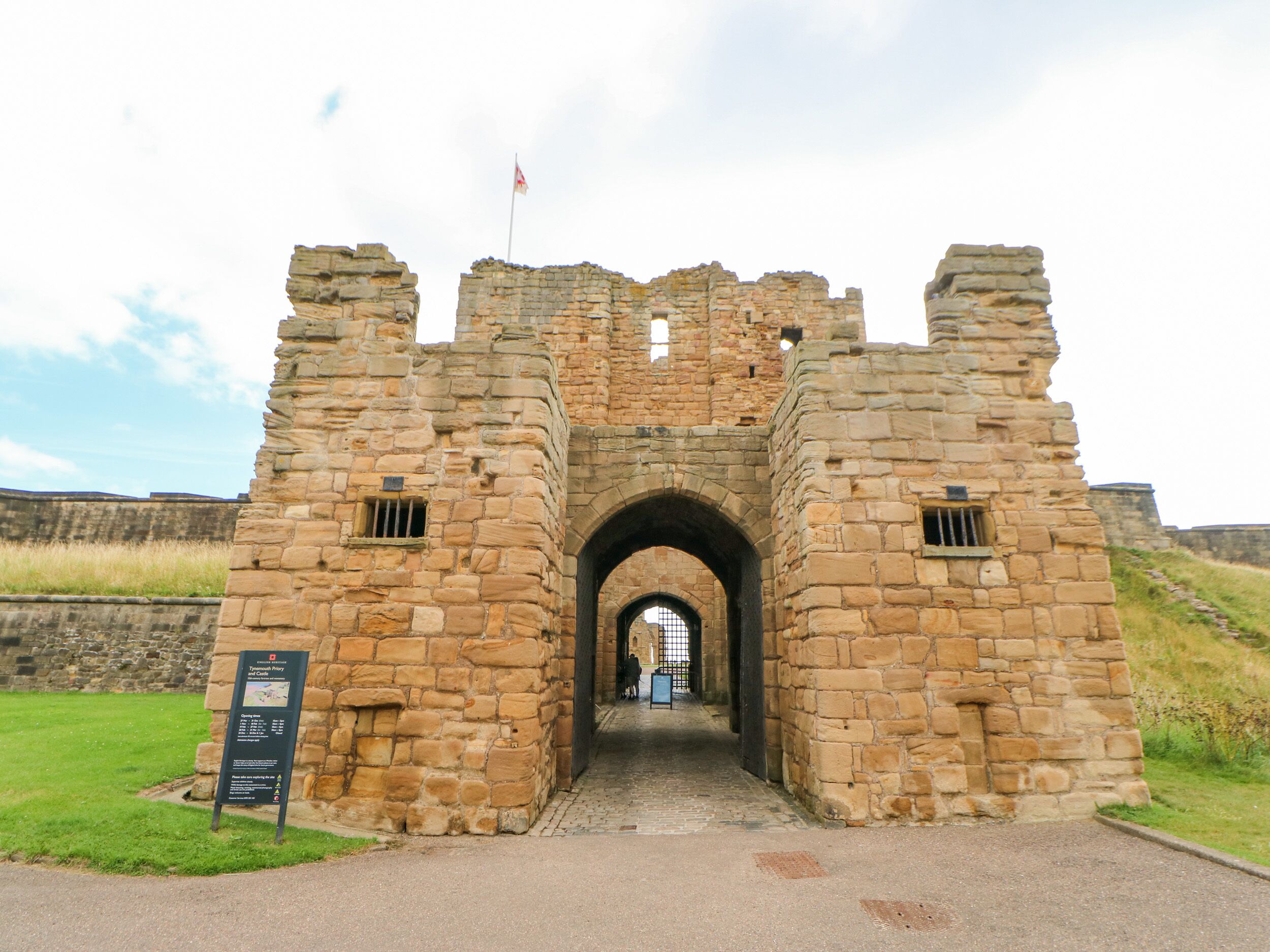 A stone archway leading into a castle ruin with a flag on top.