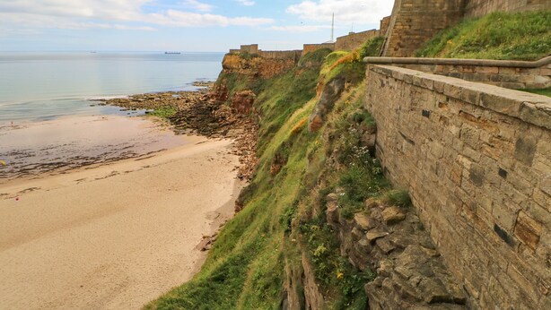 A coastal landscape with a sandy beach, a stone wall, and a grassy cliff. - 2 Hartburn Road (North Shields)