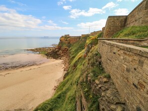 A coastal landscape with a sandy beach, a stone wall, and a grassy cliff. - 2 Hartburn Road (North Shields)
