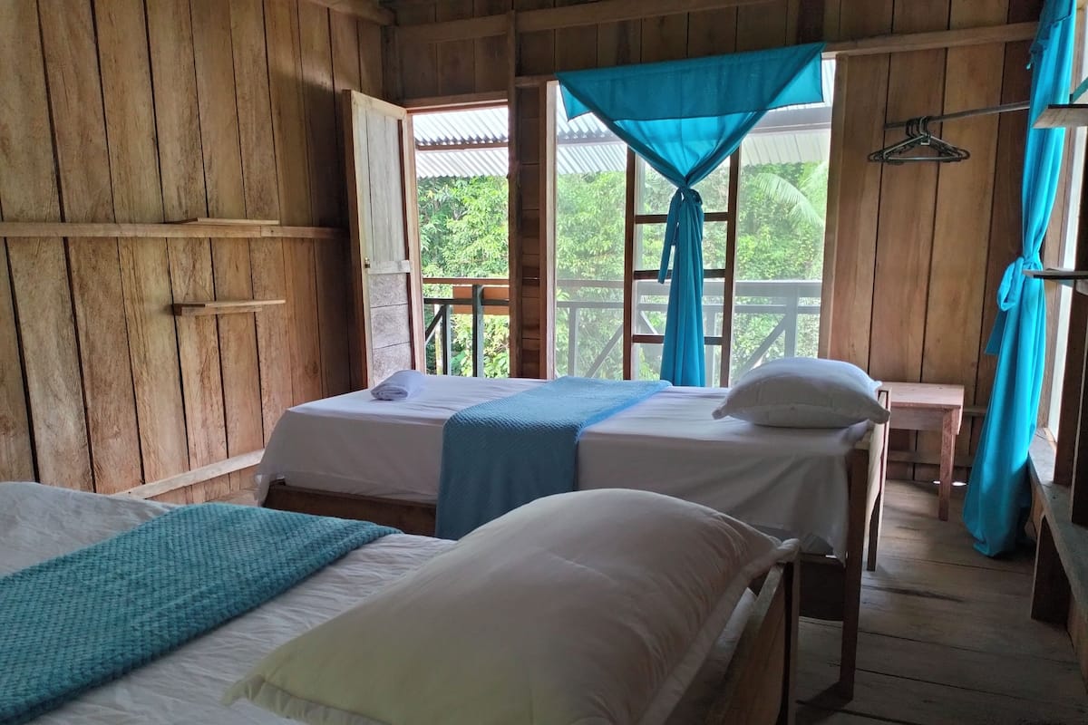 A wooden cabin with two beds, a small table, and a window with a blue curtain.