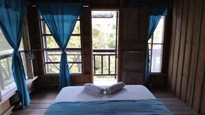 Una habitación con cama, cortinas y vistas al verdor exterior.