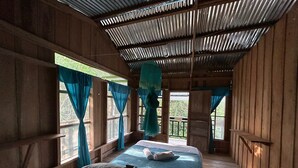 Una habitación de madera con una cama, cortinas y vistas al verdor.
