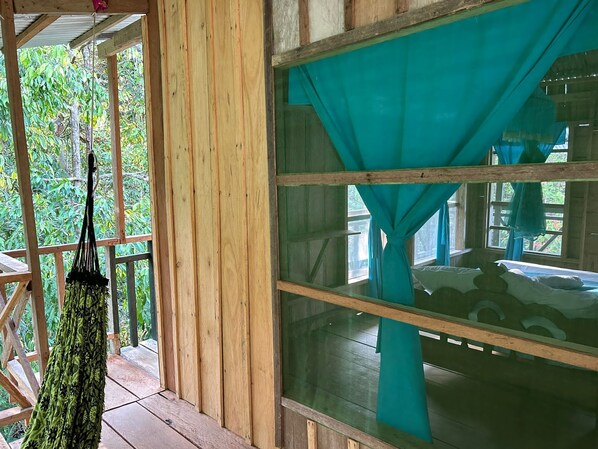A wooden cabin with a large window covered by a teal curtain. - Cabañas Ecológicas Mu'ü (Leticia)