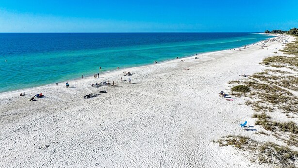 Une vaste plage de sable fin bordée d’une eau turquoise et limpide, avec quelques personnes et quelques chaises de plage.