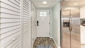 Un couloir avec une porte blanche, un réfrigérateur en acier inoxydable et un tapis à motifs.