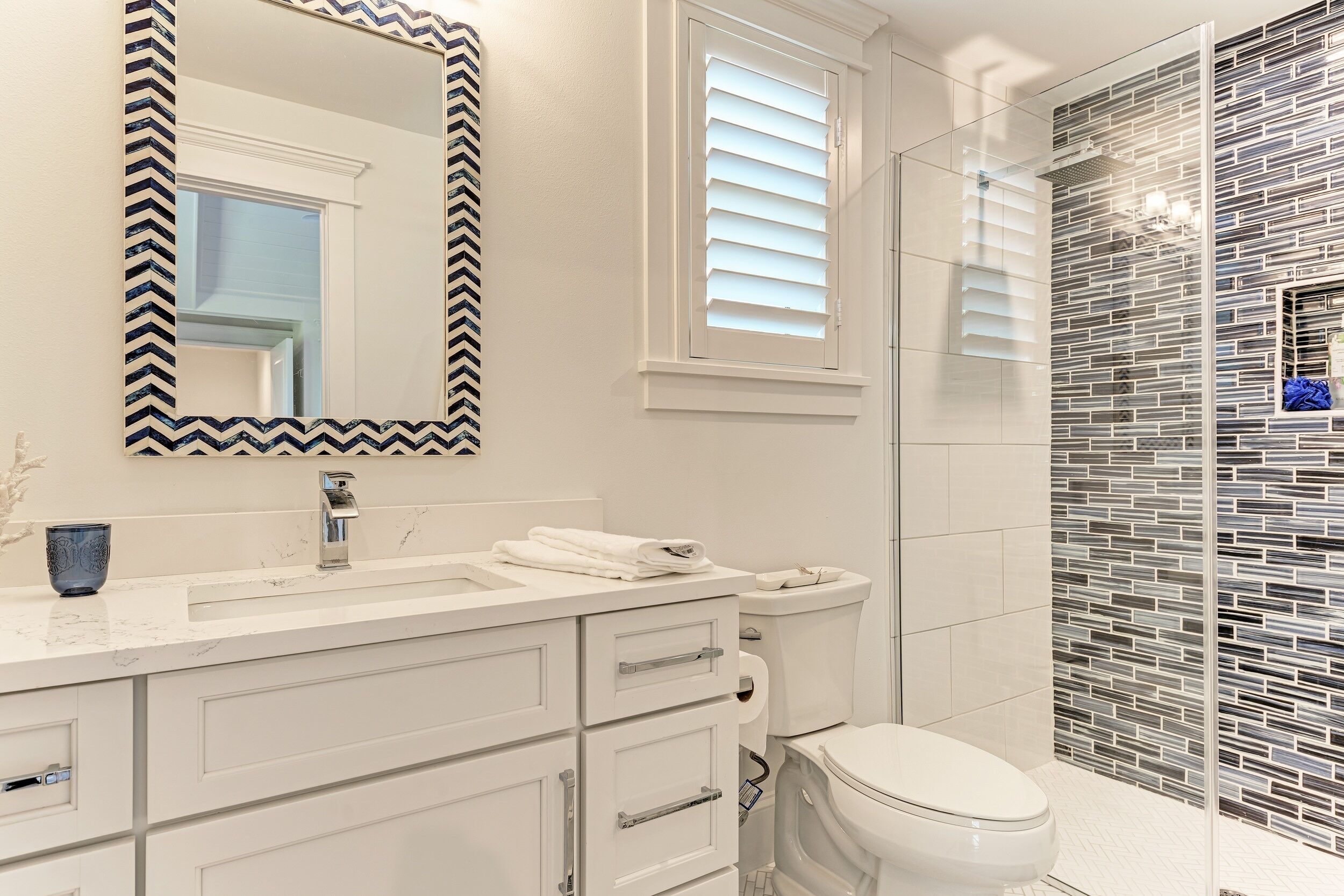 A bathroom with a white vanity, a mirror with a black and white border, a toilet, and a shower area with a tiled wall.