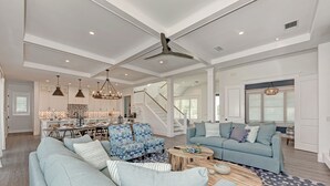 A spacious living room with a large sofa, blue patterned chairs, and a coffee table. A staircase leads to an upper level. - Just Beachy managed by Beach Retreats (Holmes Beach)