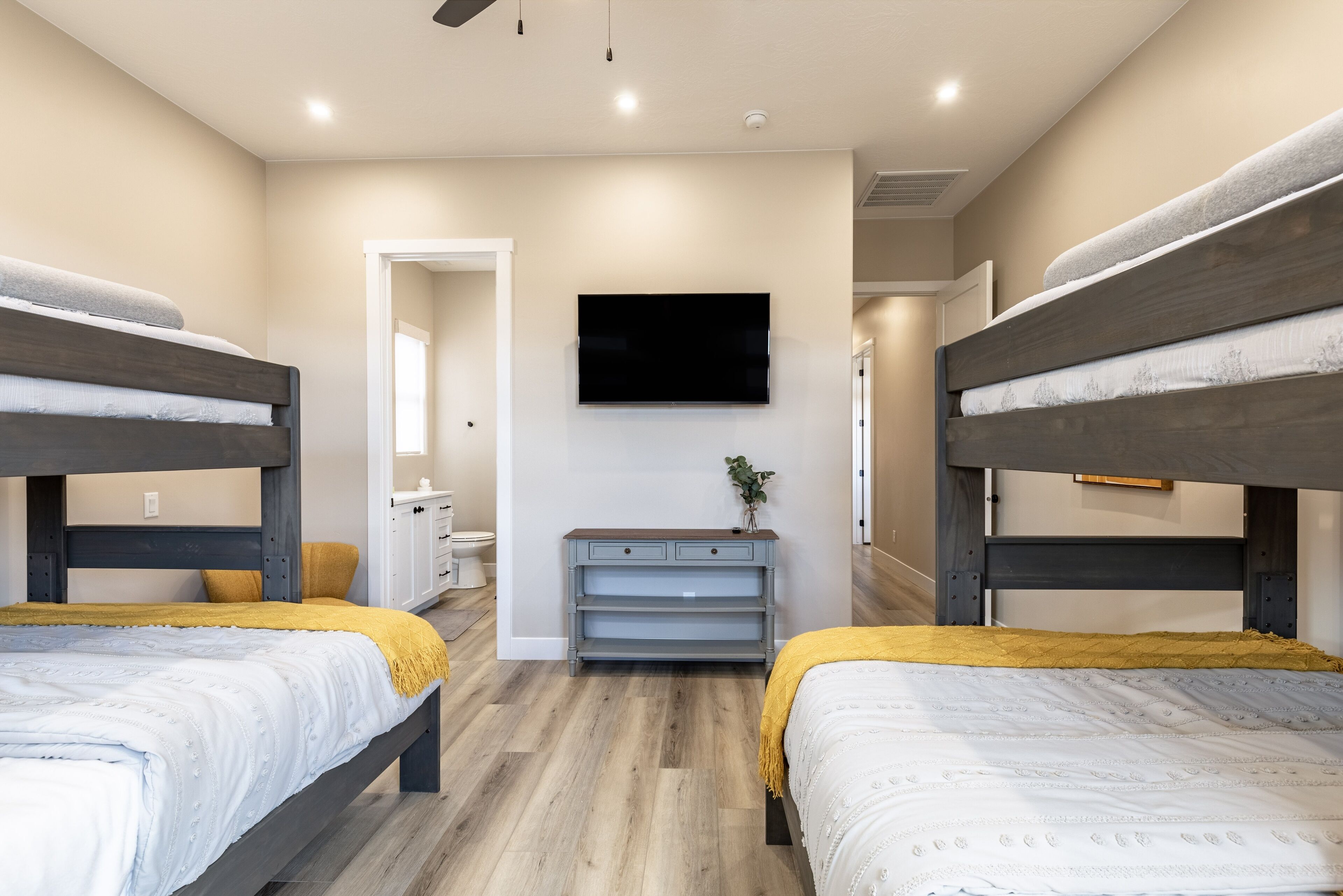 A bedroom with two bunk beds, a TV mounted on the wall, a small desk, and a plant.