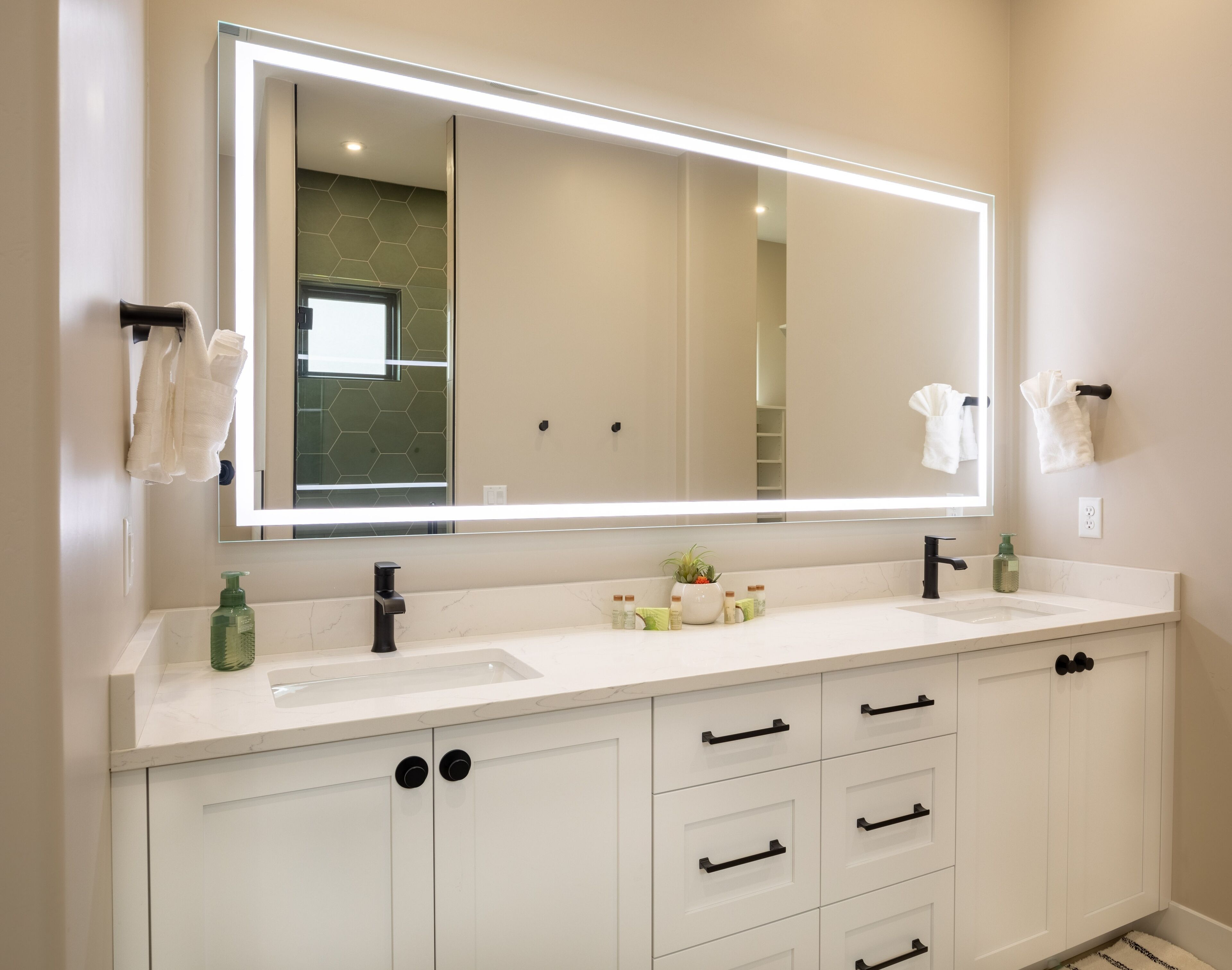 Une salle de bain moderne avec un grand miroir, deux lavabos et un meuble-lavabo avec des placards.