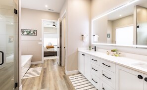 A modern bathroom with a large mirror, white cabinetry, and a wooden floor. - Sunshine Retreat 2 Bedroom Home by RedAwning (Washington)