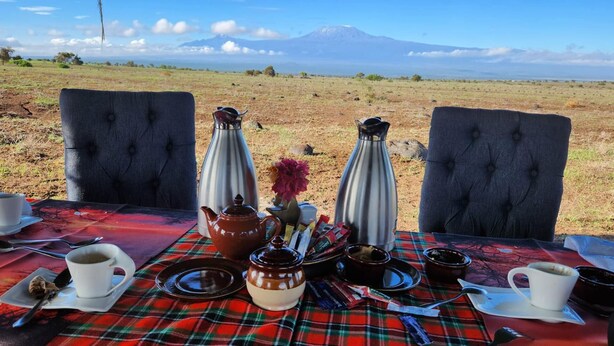Disposição para refeição com uma mesa posta para dois, incluindo toalha xadrez, bule de chá, xícaras e vista para uma montanha ao fundo.