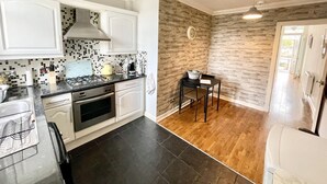 A modern kitchen with white cabinets, a black countertop, and a stone wall backsplash. - Ground Floor Victorian Apartment (Coatbridge)