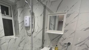 A modern bathroom with a glass shower enclosure, a white sink with a mirror above it, and a toilet. - Luxury Detached Studio Apartment in Luton (Luton)