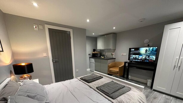 A modern bedroom with a bed, bedside lamp, and a TV in the corner. - Luxury Detached Studio Apartment in Luton (Luton)