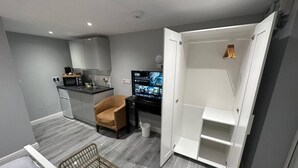 A compact living space with a kitchenette, a TV, a chair, and a wardrobe. - Luxury Detached Studio Apartment in Luton (Luton)