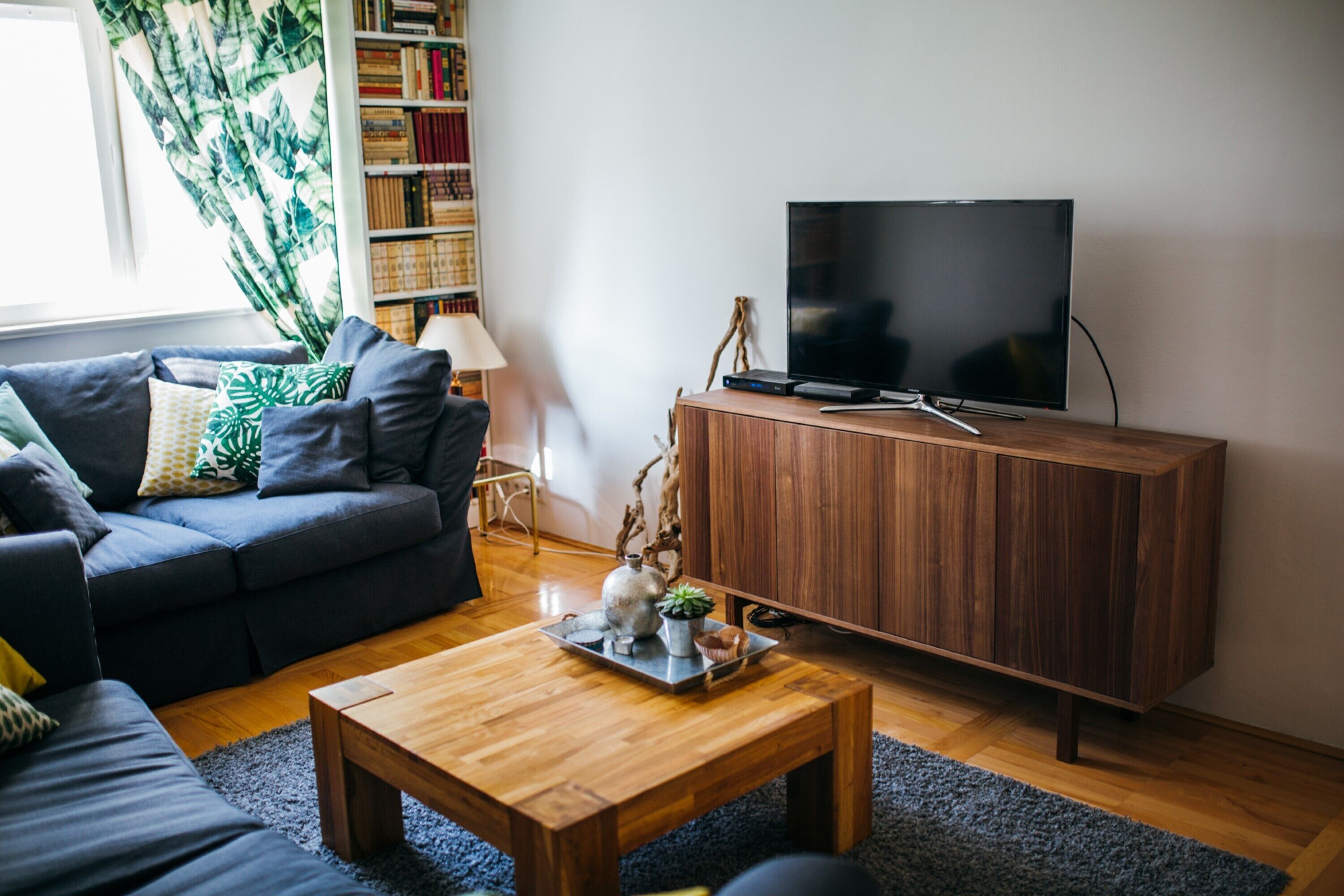 A modern living room with a dark sofa, a wooden coffee table, a flat-screen TV on a wooden cabinet, and a bookshelf filled with books.