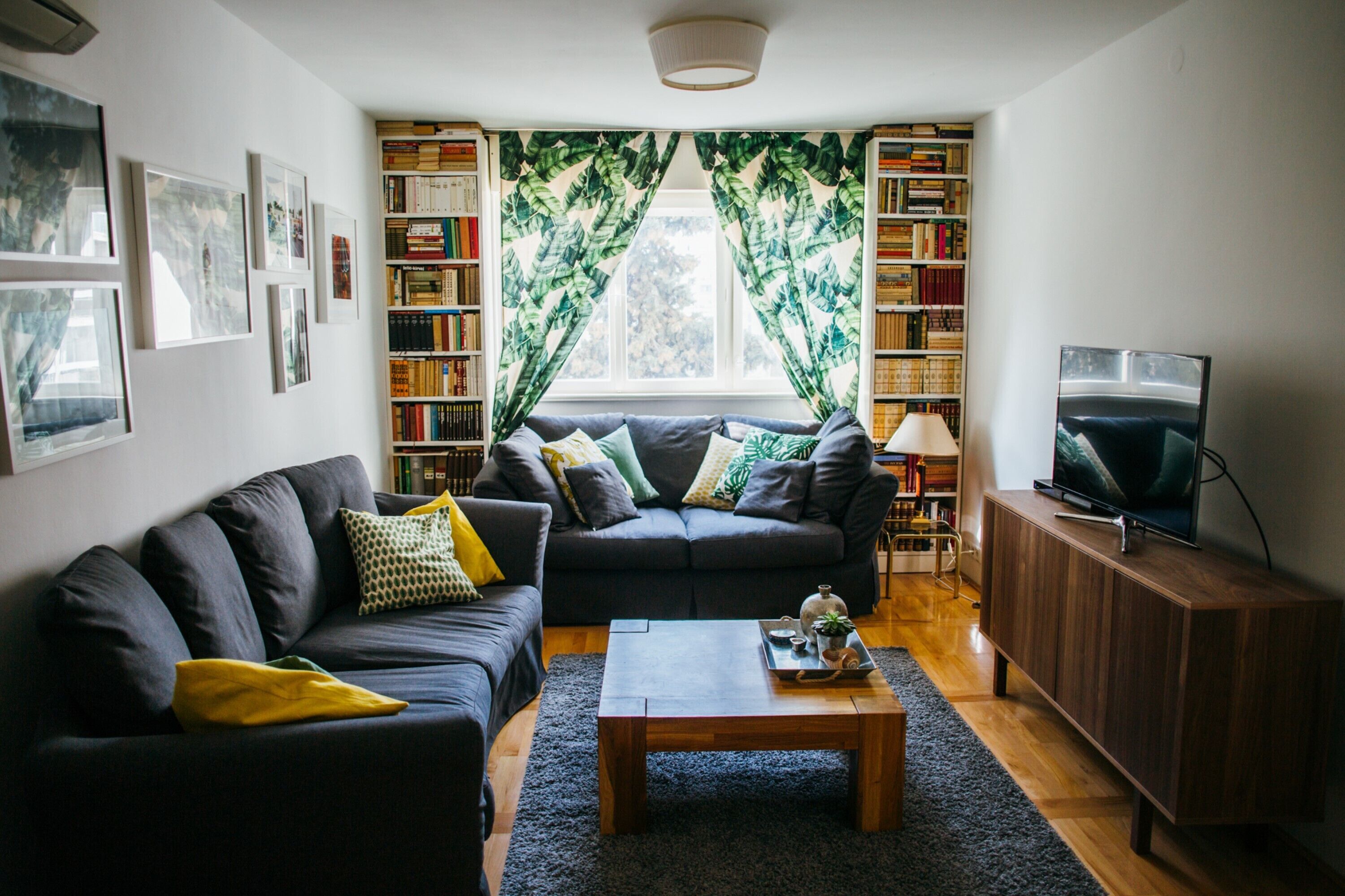 A living room with a dark sofa, a coffee table, a bookshelf, and a television.