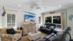 A living room with a sofa, armchairs, a coffee table, and a TV on the wall.