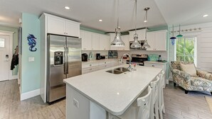 A modern kitchen with a large island, stainless steel appliances, pendant lighting, and a view of the outdoors.
