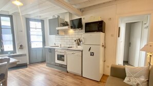 A compact kitchen with a microwave, oven, and dishwasher, a dining area with a table and chairs, and a sofa with cushions. - La Maison du Bonheur, une Ancienne Maison de Pêcheur Pour 3 Personnes (Le Crotoy)