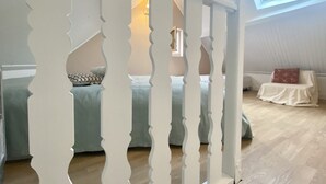 A bedroom with a sloped ceiling, a bed with patterned bedding, a white chair, and a skylight. - La Maison du Bonheur, une Ancienne Maison de Pêcheur Pour 3 Personnes (Le Crotoy)