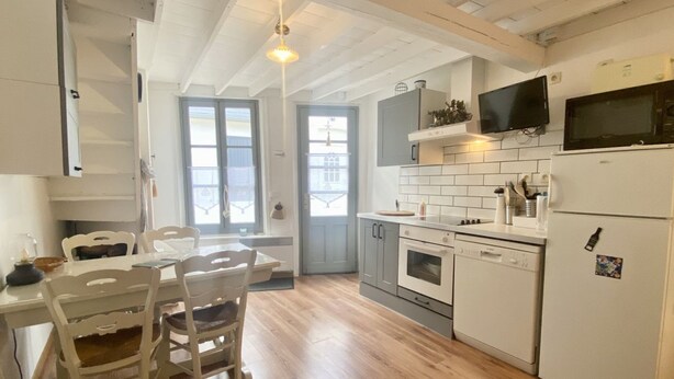 A kitchen with white cabinets, a microwave, a refrigerator, and a dining area with chairs and a table. - La Maison du Bonheur, une Ancienne Maison de Pêcheur Pour 3 Personnes (Le Crotoy)