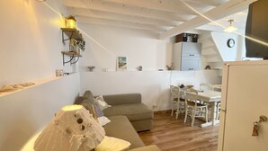 A cozy living area with a sofa, a dining table with chairs, a kitchen with cabinets, and a lamp. - La Maison du Bonheur, une Ancienne Maison de Pêcheur Pour 3 Personnes (Le Crotoy)