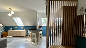 Ett rum i loftstil med högt i tak, en matplats med barstolar, en soffa och en säng med ett randigt sänggavel.