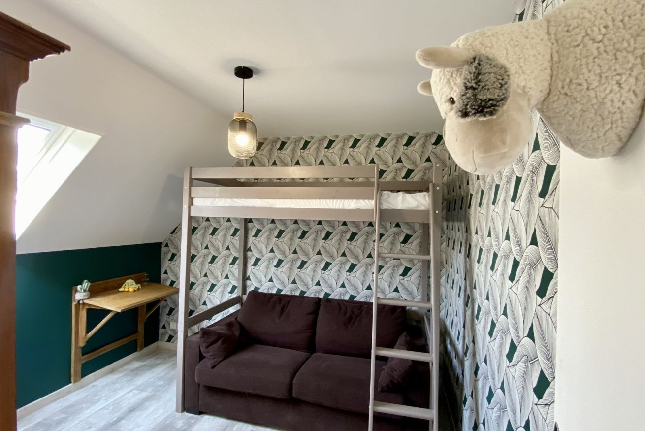 A room with a bunk bed, a sofa, a desk, and a hanging sheep decoration.