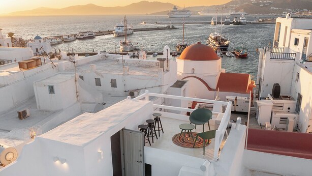 Una terrazza sul tetto con vista sul mare e sulle barche, edifici bianchi e una struttura a cupola rossa.