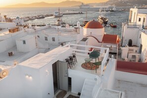 Eine Dachterrasse mit Blick auf das Meer und Boote, weiße Gebäude und eine rot Kuppelartige Struktur.