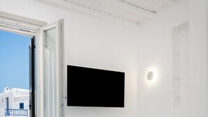Una camera da letto con un letto, una TV fissata al muro e una finestra con persiana aperta.