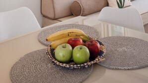 Un soggiorno moderno con un divano beige, un tavolino da caffè bianco con una ciotola di frutta e opere d'arte incorniciate appese al muro.