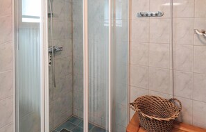 Eine begehbare Dusche mit Glastrennwand, einer Handbrause, einem Metallhandtuchhalter und einem Korbwäscher auf einem Holzregal.