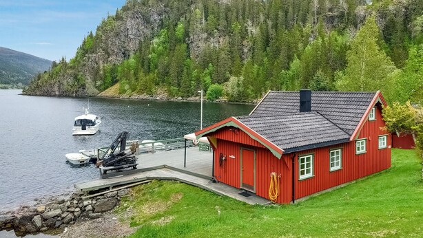 Una baita rossa in riva a un lago, con un pontile e una barca.
