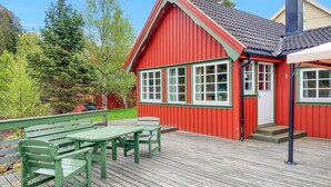 Un edificio di legno rosso con tetto in tegole, una terrazza in legno con panchine e vista su alberi e una barca sullo sfondo.
