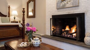 Una habitación con chimenea, una cama, una mesita de noche, una lámpara y un florero con flores.