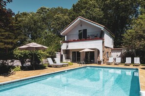 Una casa de dos pisos con piscina, mobiliario exterior y un balcón.