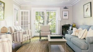 Una sala de estar con sillones a rayas, un sofá, una mesa de centro y una puerta que da a un jardín.