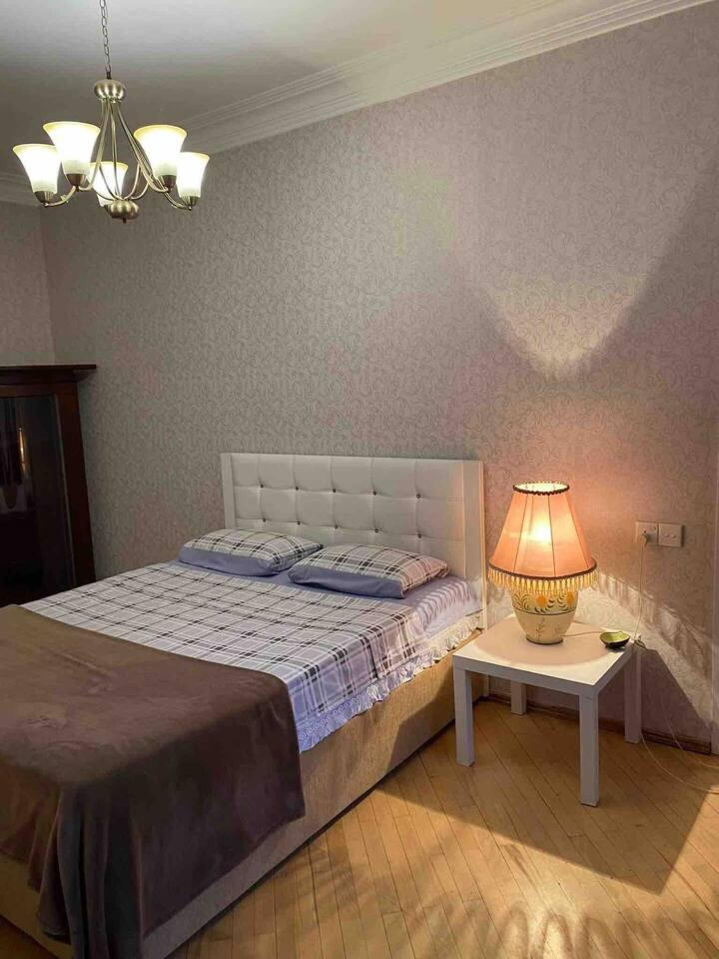 Une chambre à coucher avec un lit, une table de chevet, une lampe et un lustre.