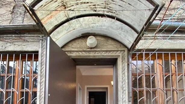 Ein Gebäudeeingang mit einer gewölbten Arkade, Fensterläden aus Metall und einem gefliesten Boden.
