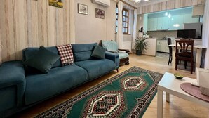 Ein Wohnzimmer mit einer Couch, eine Essecke mit Tisch und Stühlen, eine Küche mit Schränken und einer Arbeitsplatte sowie ein gemustertes Teppich.