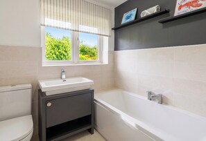 Une salle de bain comprenant des toilettes, un lavabo et une baignoire, une fenêtre avec des stores et une étagère sur laquelle est posée une photo encadrée.